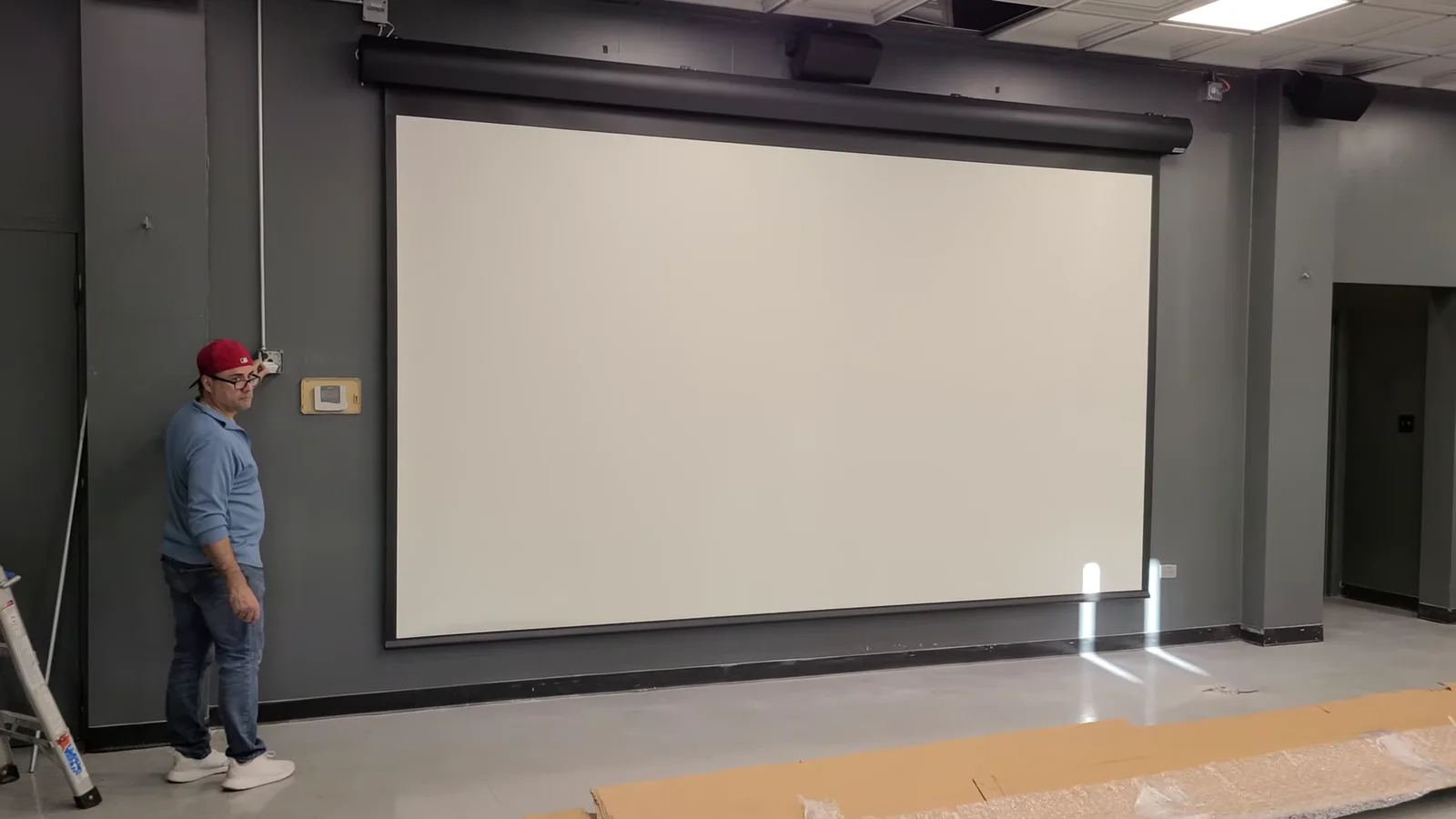 Denali Tech technician standing beside a deployed 190-inch motorized projection screen