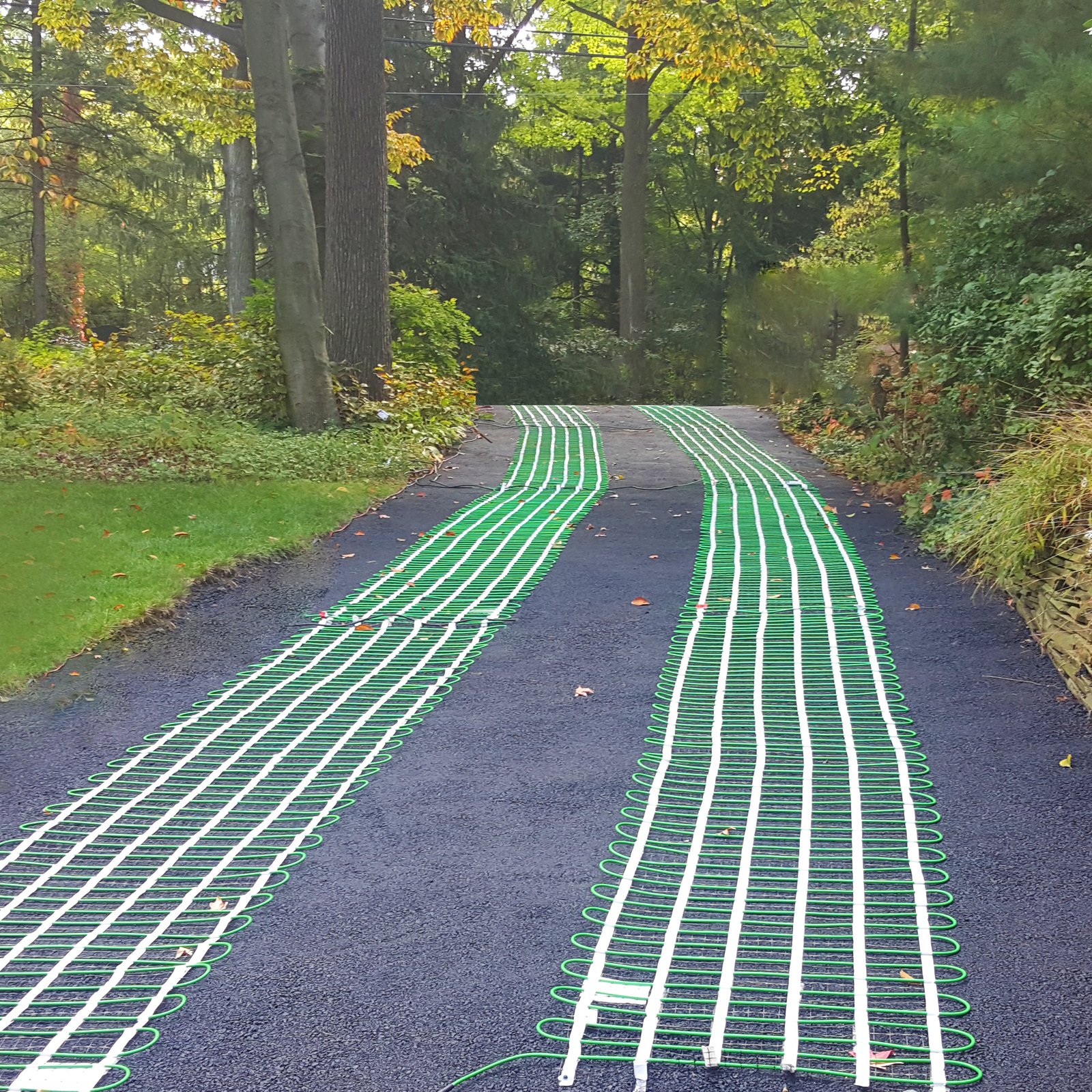 Electric snow-melting mats arranged as heated tire tracks before a new asphalt layer