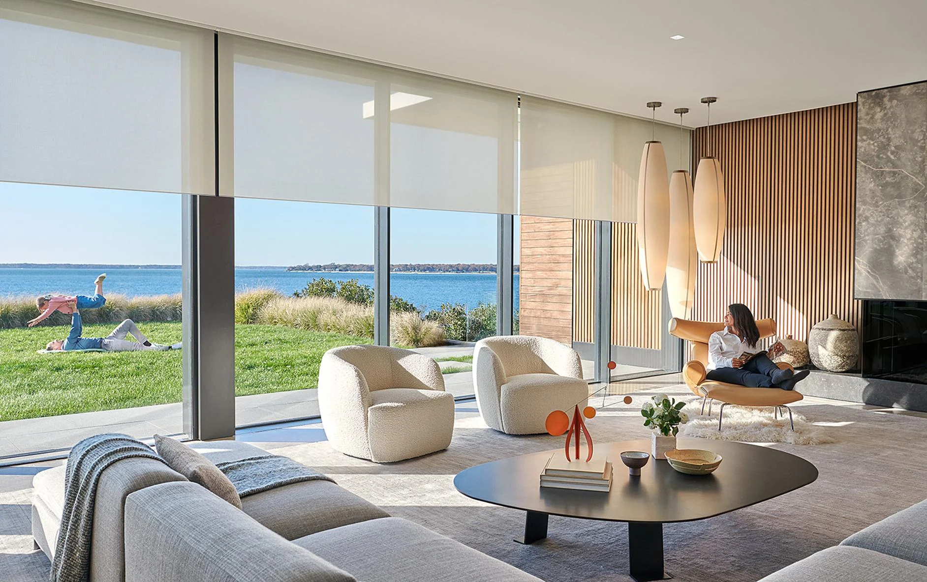 Bright modern living room with large Lutron roller shades, architectural lighting and waterfront view